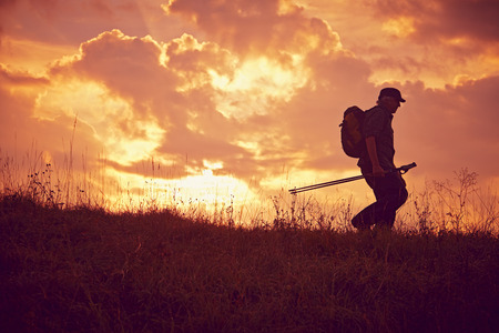Hiker with Cap and sticks on meadow downhill walkingの写真素材