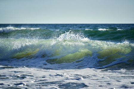 Wave just breaking and white on the sea in backlight and sprayの写真素材