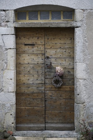 Wooden old and dark wood door and metal rivets with wooden wreath on a buildingの写真素材