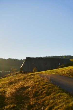 Farmhouse with meadow at the forest with mountain slope and house in the sun in autumn in backlightの写真素材
