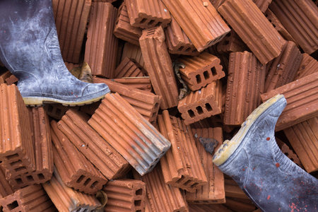 dirty rubber boot on pile of orange bricks for construction