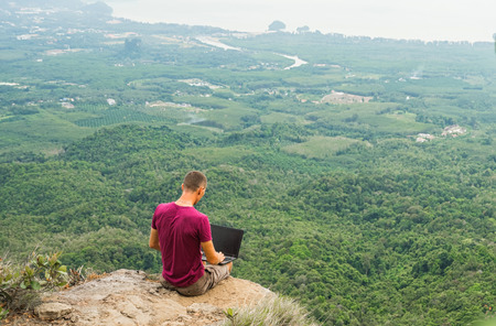 Man working with laptop sitting on the rocky mountain on beautiful scenic clif background. Thailand. Krabi .の写真素材