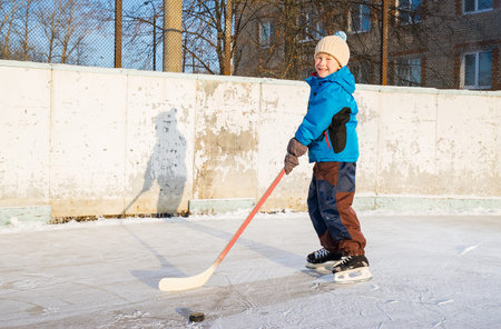 Winter time. Young smiling boy playing ice hockey on an outdoor ice rink.