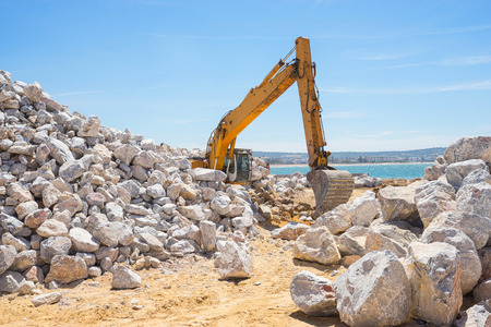 Mechanical excavator working on coast with big stones.の写真素材