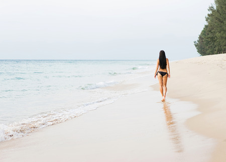 Vacation on the sea. Young sexy caucasian woman walk alone on ocean beach. Back view.の写真素材