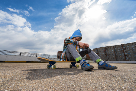 Boy sitting on skateboard and thinking about somethingの写真素材