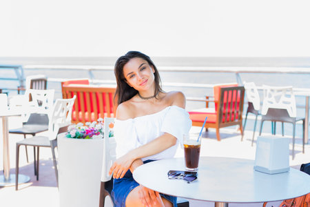 Woman sitting in cafe with ice coffee with sky and sea background. Selective focus.