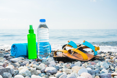 Vacation concept. Essentials on the sea beach. Bottle of drinking water,  towel,  woman shoes and sun protected cream.の写真素材