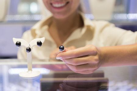 Seller in jewerly shop show set with black pearls. Focus on pearl on the ring in hand.