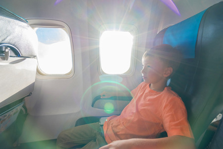 Kid sitting in the airplane durring fly. Sunrays and subeam from plane window. Selective focus.の写真素材