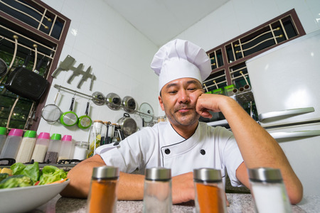 Asian chef sitting on the kitchen and thinking. In the front of picture  blured spices.の写真素材