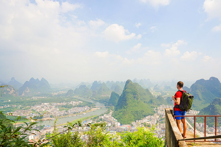 Hiker with backpack enjoying view from top of the hill with beautiful view on Yangshuo city with mountains around. Yangshuo, China.の写真素材
