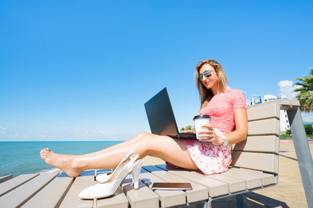 Woman sitting on the beach chiar  with laptop , smartphone, white shoes, and drink coffee.の写真素材