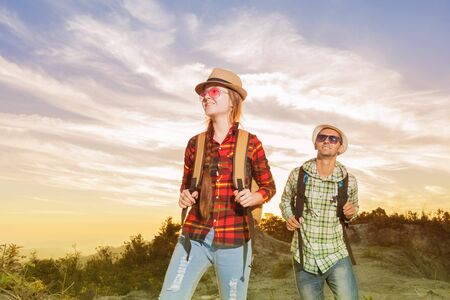 Happy hikers with backpacks walking in mountains at sunset.