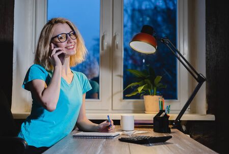 Happy young woman with phone sitting at the table in room.の写真素材