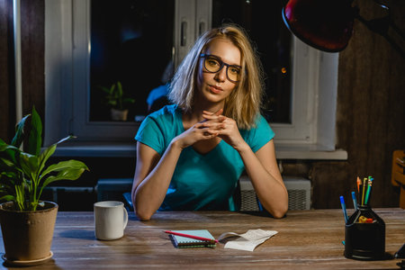 Young woman in glasses sitting at table with notebook, papers, coffee cup. Color toned.の写真素材