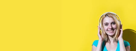Young woman having fun while listening to music using earphones isolated over yellow background. Banner.の写真素材