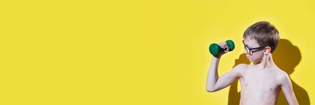 Small boy in glasses holding dumbbell in hand. Sport and fitness concept. Banner edition.	の写真素材