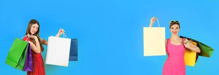 Two young and happy women with shopping bags on blue background. Banner edition.の写真素材