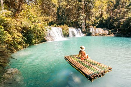 Woman in bikini and hat sitting on bamboo raft and enjoying view on waterfall.の写真素材