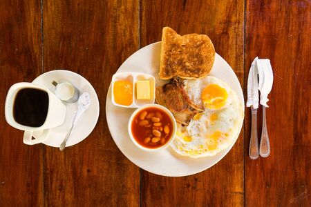  Breakfast with eggs, pork, toast, beans, butter, jam and coffee. Wood background. Selective focus.の写真素材