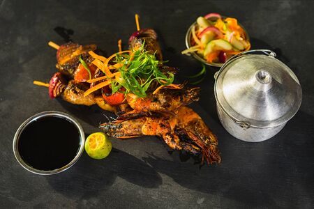 BBQs from fish, squid and shrimp with sauce, lime and salad on black wooden background. Selective focus.の写真素材