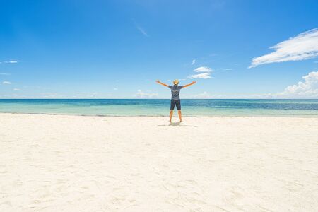 Happy man in hat with raised hands on the beach. Back view. Vacation and holidays on the tropic countries concept.の写真素材
