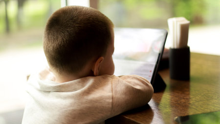 Banner A child watches cartoons in a cafe. Boy with tablet in a restaurant