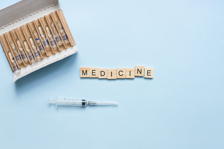 The word medicine from wooden letters. Flat lay ampoules and syringe on a blue background. treatment, vaccinationの写真素材