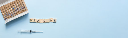 Banner The word medicine from wooden letters. Flat lay ampoules and syringe on a blue background. treatment, vaccinationの写真素材
