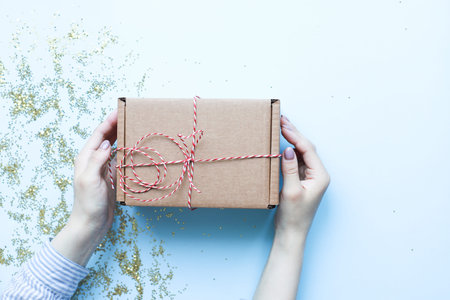 Hands holding a craft gift. Christmas gift on a blue background. Gift with red and white rope