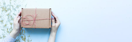 Banner Hands holding a craft gift. Christmas gift on a blue background. Gift with red and white ropeの写真素材