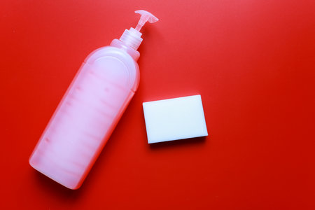 Flat lay dishwashing detergent and sponge on red background. Cleanliness cleaningの写真素材