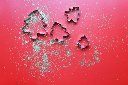 Flay lay molds for cookies in the shape of Christmas trees on a red background with sparklesの写真素材
