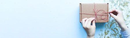 Banner Wrap gifts. Flat lay christmas present. Hands holding a craft box with a bow
