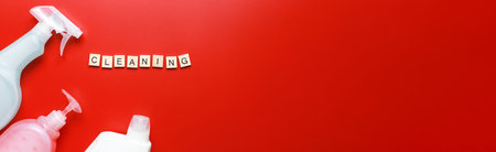 Banner Flat lay cleaning products, cleaning spray on red background and sponges. Word cleaning from wooden lettersの写真素材