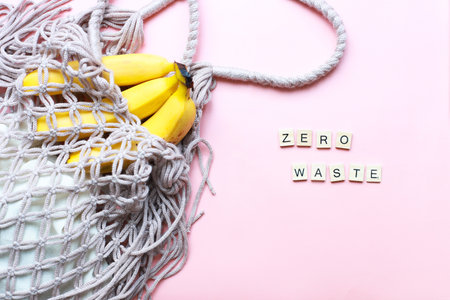 Flat lay bananas in a mesh bag. Zero west from wooden letters on a pink background. Reasonable consumptionの写真素材