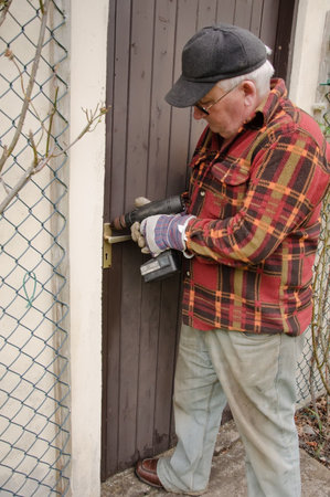 senior male repairing a wooden door latch with drill