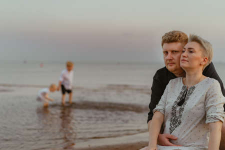 lovely caucaisan family: man hugging g his pregnant wife. Kids playing in the sea at sunset. high quality photoの写真素材