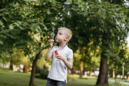 cute caucasian blond boy blowing soap bubbles in park. High quality photo. happy childhood conceptの写真素材