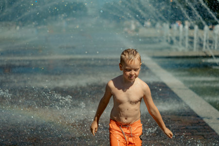 cute caucasian boy wearing swimming shorts running in a fountain. high quality photoの写真素材
