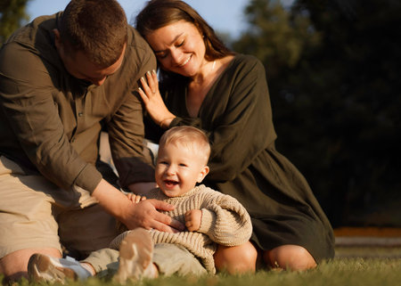 happy family sitting on the grass in the park. Mom putting head on husband's shoulder. baby boy...