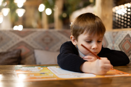 cute little boy drawing with color pencils sitting at the table in restaurant. Image with selective...