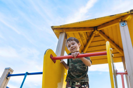 Cute Caucasian boy on playground on summer day. Blue sky on background Image with selective focus