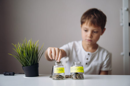 little caucasian boy putting coin into glass bottle at the table. Kid saving money for the future...