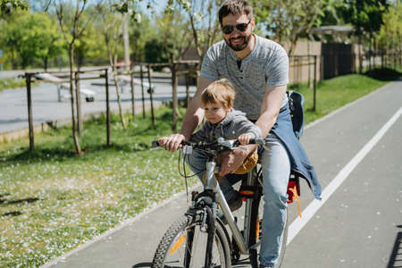 father and son cycling together on one bicycle along bike lane. father's day concept. Image with selective focus. high quality photoの写真素材