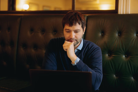 Thoughtful businessman working on new online project on laptop computer sitting at the table in...