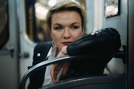 closeup portrait of young caucasian short haired blond woman wearing leather jacket sitting in car of metro, looking aside. Image with selective focus. high quality photoの写真素材