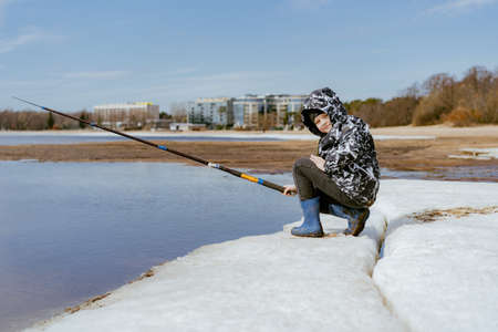 Cute little caucasian boy holding a fishing rod looking into distance on sea side on spring day. blue cloudy sky background. Image with selective focusの写真素材