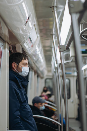 caucasian man wearing medicine mask standing inmetro car leaning on door. high quality photo